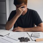 Asian men are stressed about financial problems, with invoices and calculators placed on the table while having stress on problems with home expenses.